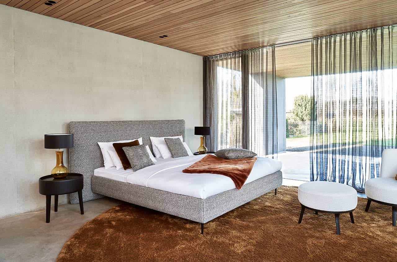 Helles Schlafzimmer mit grauem Polsterbett.